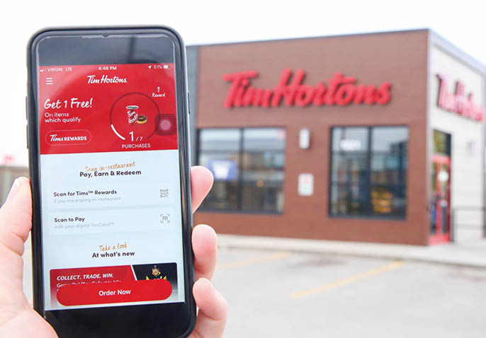 Winnipeg; Manitoba   Canada - October 8; 2019: Close-up of the Tim Hortons App with a Tim Hortons Store in the Background 