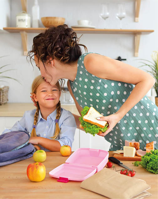 Beautiful brunette mother and her daughter packing healthy lunch and preparing school bag in the kitchen 