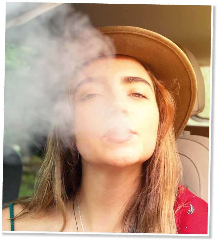 Young woman sitting in a car looking at the camera while blowing smoke from an electronic cigarette  Vaping concept