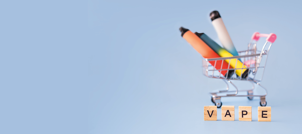 A device for vaping in a mini shopping cart on a blue background and next to the wooden letters of the word vape  the concept of vaping electronic cigarettes