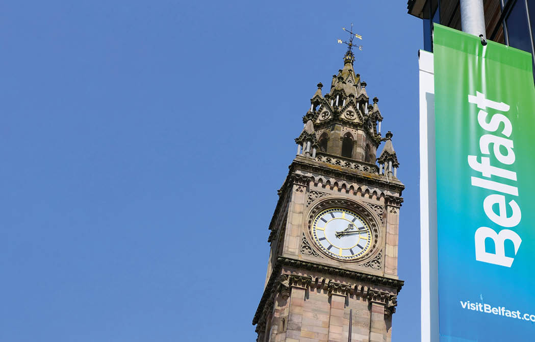 BELFAST, NORTHERN IRELAND â   JUNE 02, 2019: The Albert Memorial Clock Tower with a colorful Belfast sign for the promotion of tourism in Belfast