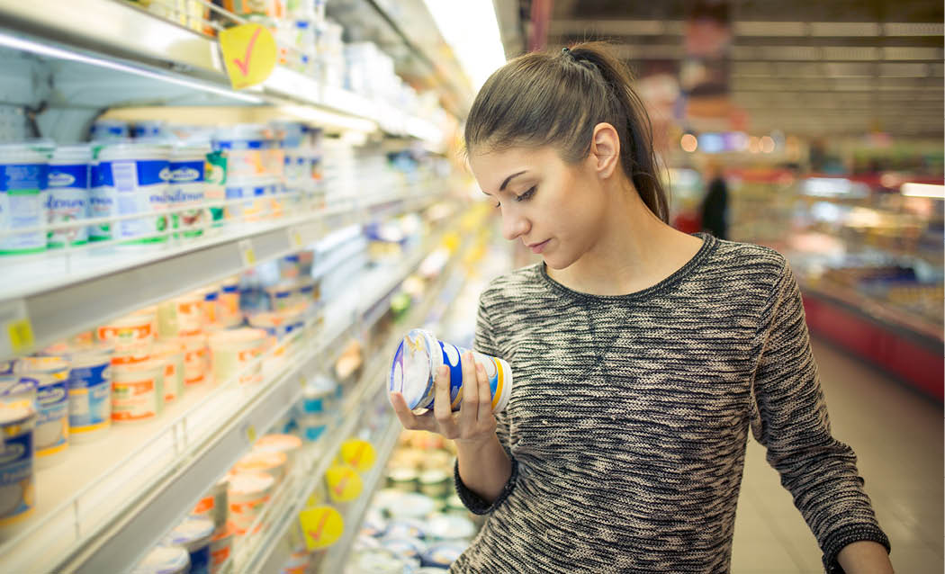Young woman reading ingredients,declaration or expiration date on a dairy product before buying it Curious woman reading nutritional values of the food Shopping in the supermarket grocery store 