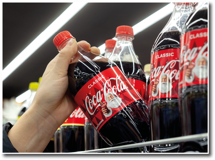 MINSK, BELARUS - December 19, 2019: Hand holds a bottle of Coca-Cola with Christmas image of Santa Claus on the label  Man shopping Coca-Cola in grocery store 