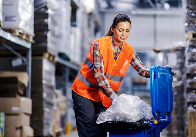 A female storage worker putting plastic bags into recycle bin.