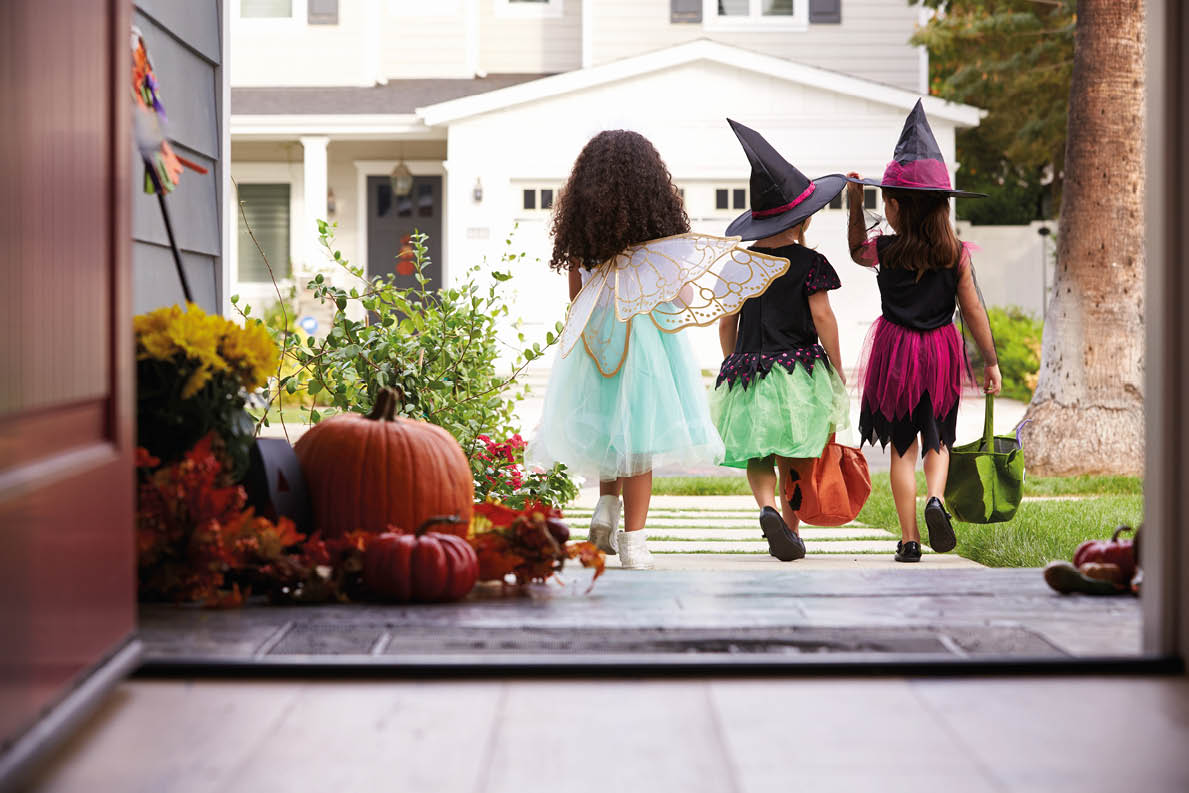 Three Children In Halloween Costumes Trick Or Treating