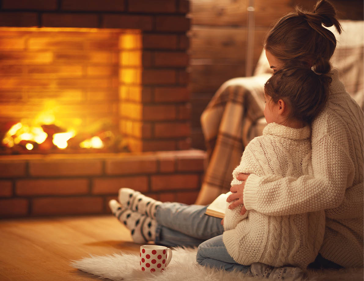family mother and child daughter hugs and warm on winter evening by fireplace