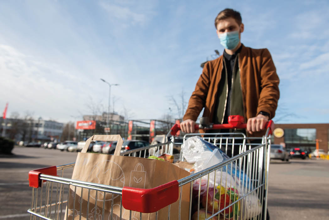 Riga, Latvia - April 20 2020: Grocery shopping Men with face mask during Coronavirus COVID-19 pandemic  Men stockpile food shopping cart outside of a grocery store  Selective focus on groceries