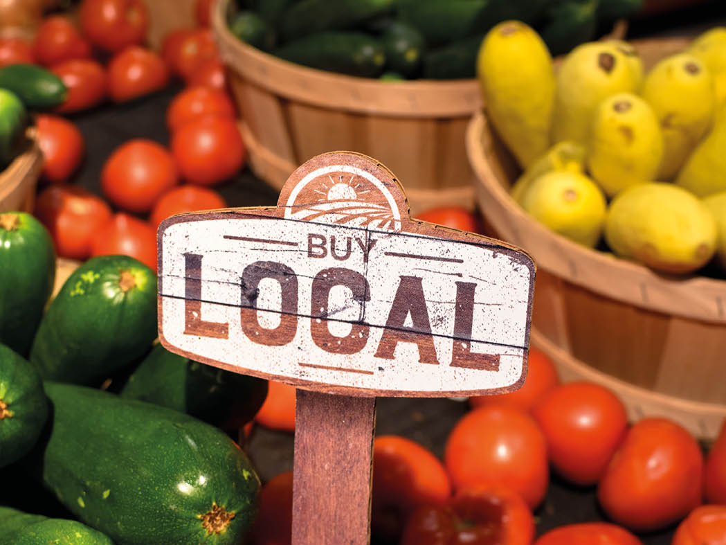 wooden sign with word signage reading buy local produce with tomatoes yellow squash and zucchini background