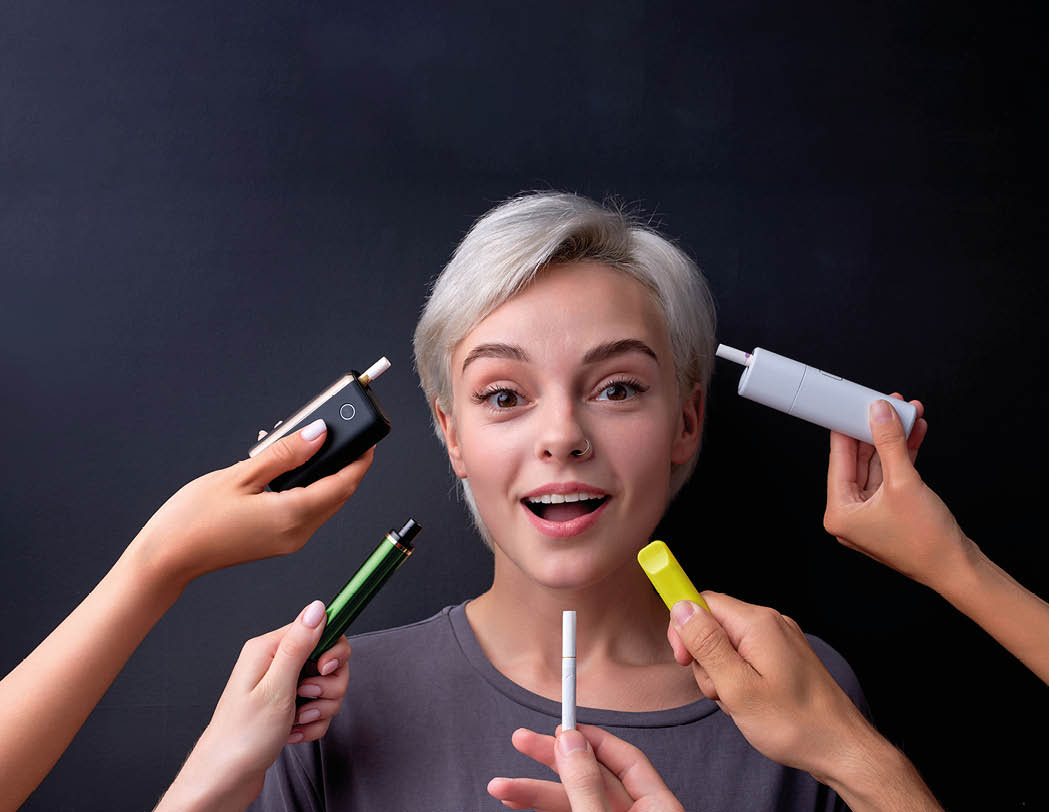 woman is happy to live in variety of choice of electronic cigarettes, choose  Joyous caucasian lady look at camera, many e-cigarette near her, posing at camera  copy space  smoking, vaping concept