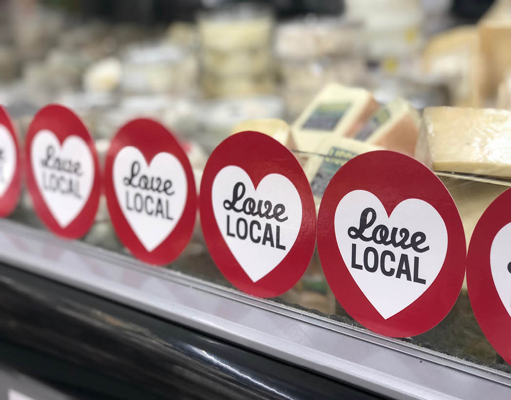 Asheville, NC   USA - May 20, 2019: This photo is of a display of local cheese that has a  Love Local  sticker on the window of the display  There are many stickers covering the window of the display 