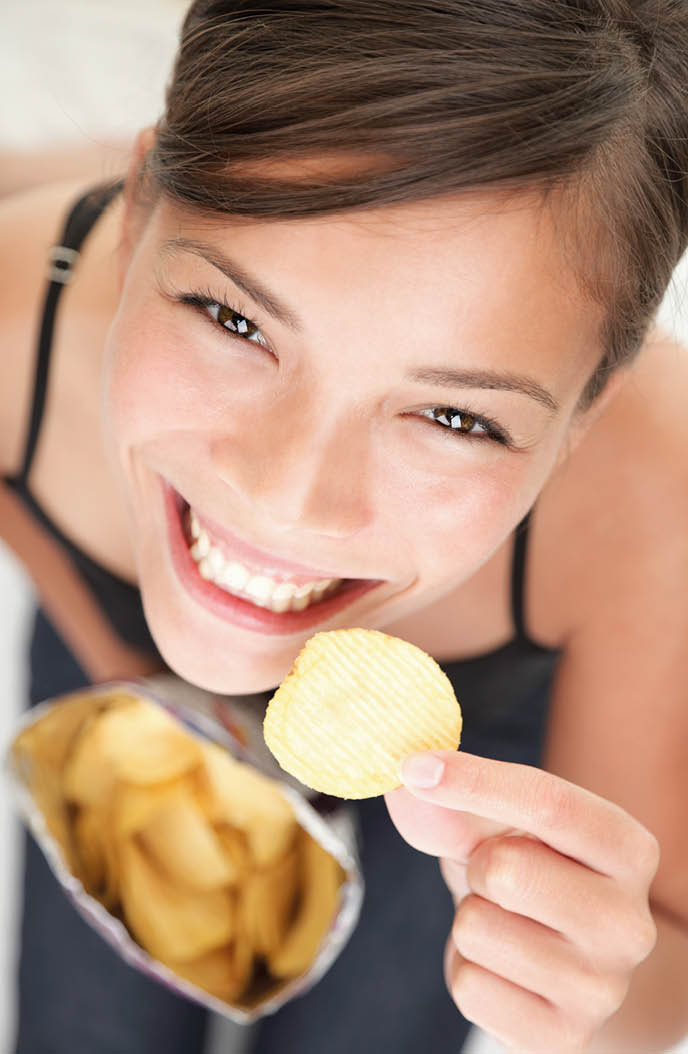 Woman eating chips  Beautiful young woman eating potato chips   crisps 