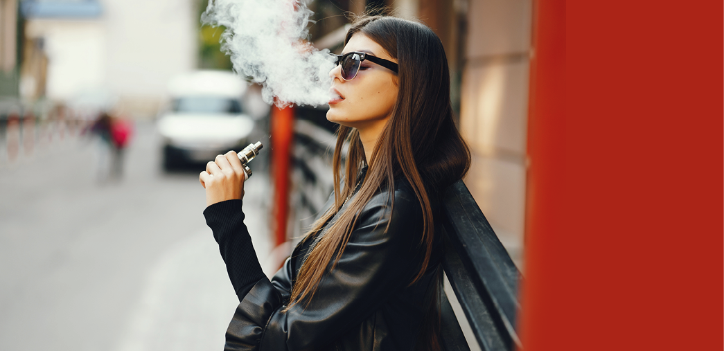 stylish girl smoking an e-cigarette as she is walking through the city