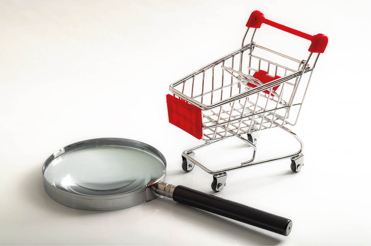 Secret shopper or mystery shopper concept with a magnifying glass and a shopping basket or trolley isolated on a white background and copy space