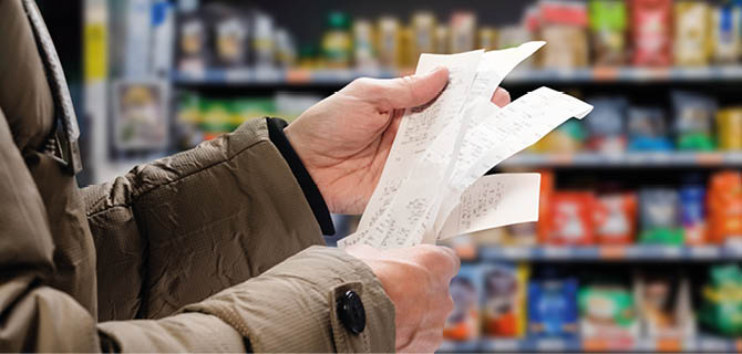 Minded man viewing receipts in supermarket and tracking prices