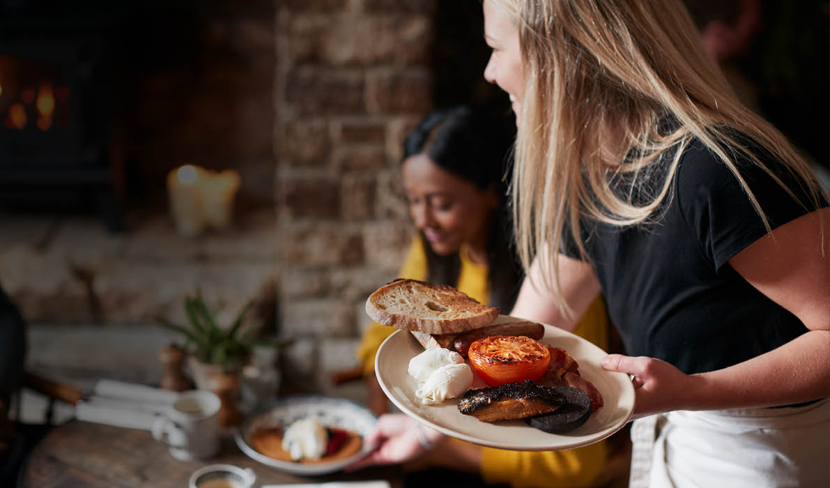 Close Up Of Waitress Working In Traditional English Pub Serving Breakfast To Guests.