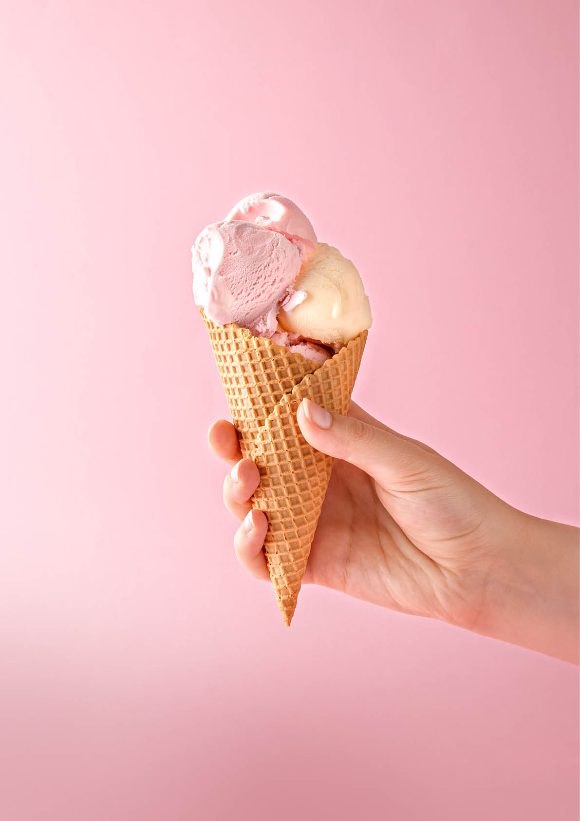 Woman hand holding an ice cream cone on a pink background. 