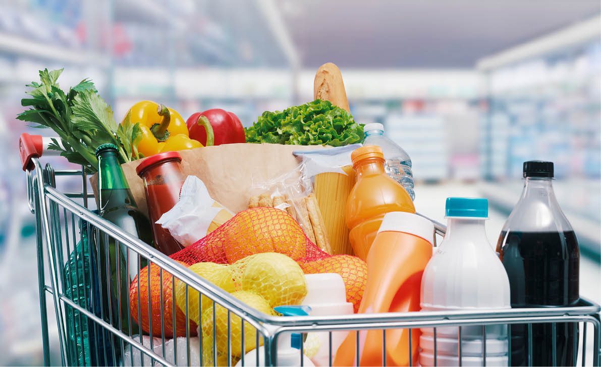 Shopping cart filled with food and drinks and supermarket shelves in the background, grocery shopping concept