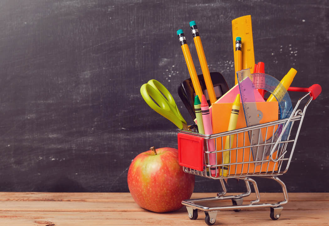 Shopping cart with school supplies over chalkboard background
