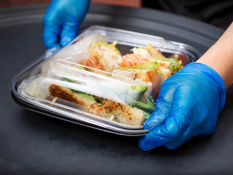 A view of an employee preparing to pack a food to-go containers, in a restaurant kitchen setting.