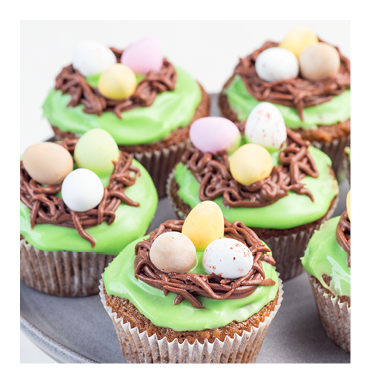 Homemade carrot cupcakes with cream cheese frosting and Easter chocolate eggs, on a gray cake stand, vertical, copy space