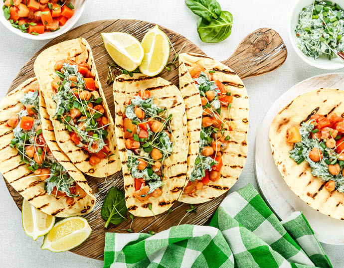 vegetarian snack of tacos with chickpea curry and sour cream sauce with parsley, spinach, green onions and sprouted flax seeds  healthy plant based food  top view on light background, flat lay