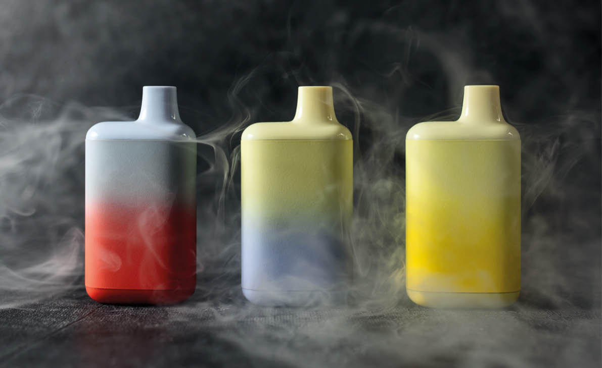 A set of multicolored disposable electronic cigarettes on a dark background stand on a table with smoke around. The concept of modern smoking, vaping and nicotine