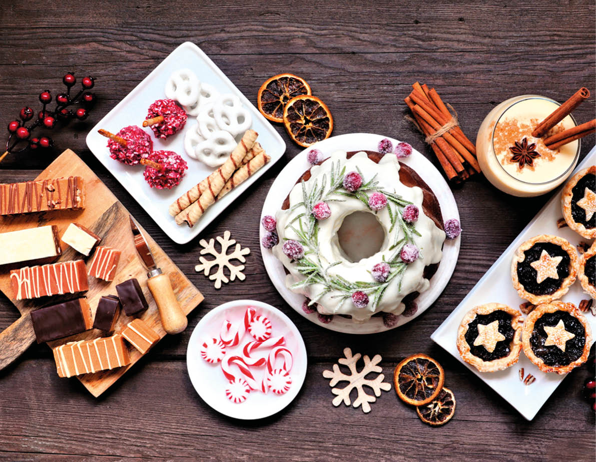 Assorted Christmas holiday desserts and sweets. Top view panoramic table scene over a rustic wood background. Bundt cake, chocolate pie, mincemeat tarts, cookies, fudge and eggnog.