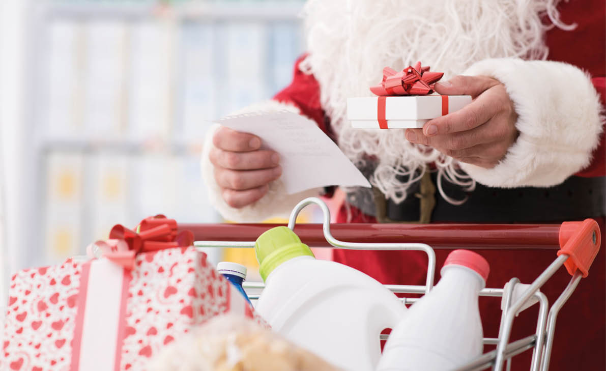 Santa Claus doing grocery shopping at the supermarket, he is pushing a full cart and checking a list, Christmas and shopping concept