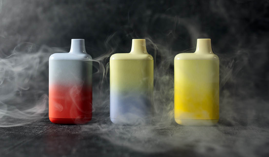 A set of multicolored disposable electronic cigarettes on a dark background stand on a table with smoke around. The concept of modern smoking, vaping and nicotine