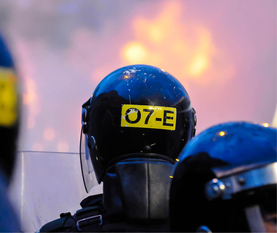 Police officers look on after a crowd starts a riot against the police and set a van on fire in Belfast