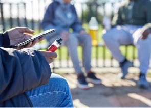 Close Up Of Teenagers With Mobile Phone Vaping and Drinking Alcohol In Park