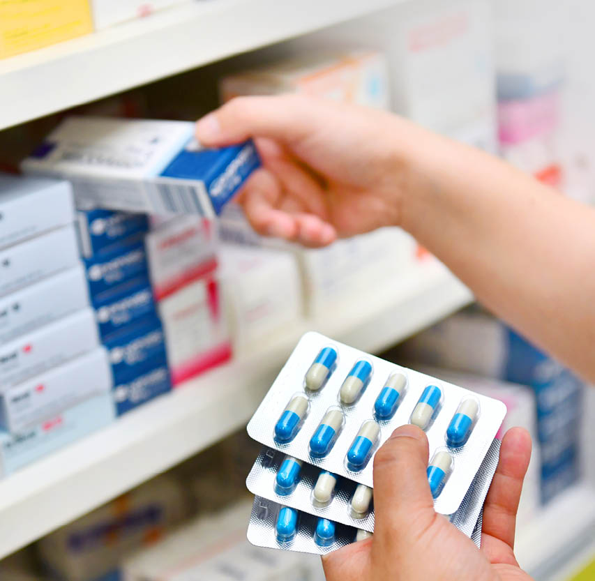 Pharmacist holding medicine box and capsule pack in pharmacy drugstore.
