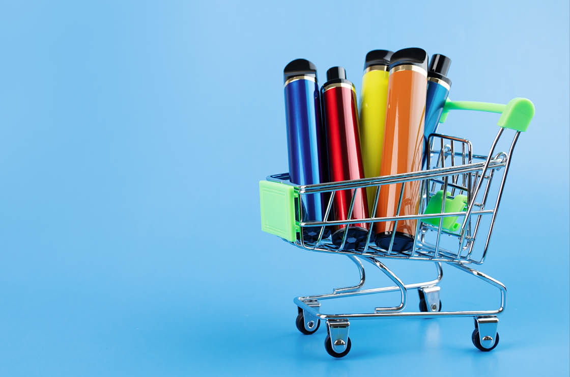 disposable electronic cigarette in a trolley,multicolored vape for smoking in a shopping cart on a blue background,copy space