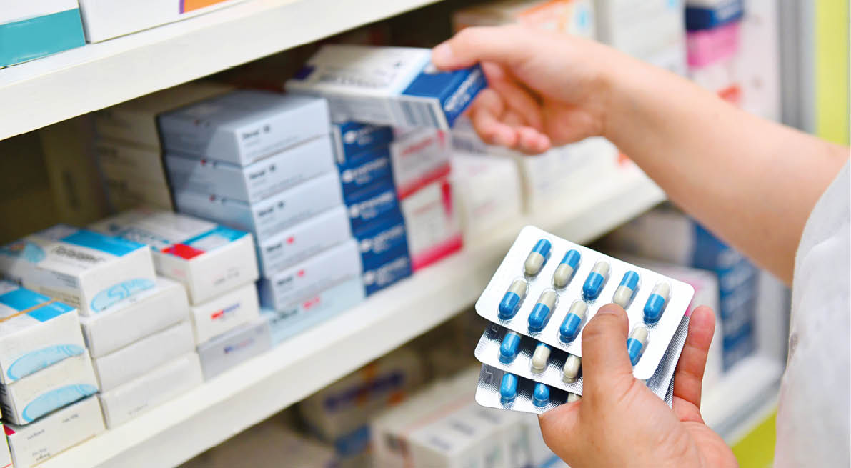 Pharmacist holding medicine box and capsule pack in pharmacy drugstore.