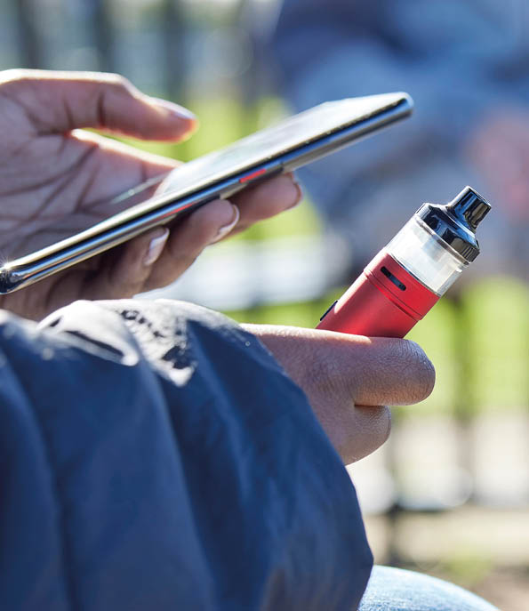 Close Up Of Teenagers With Mobile Phone Vaping and Drinking Alcohol In Park