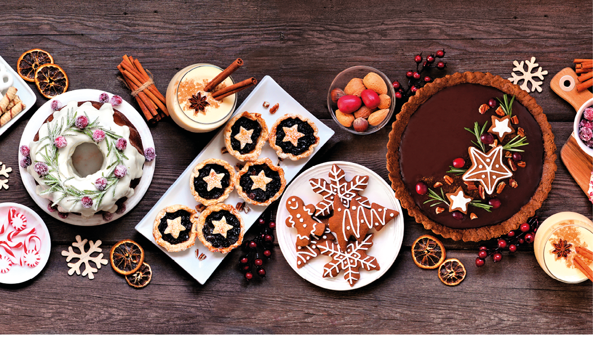 Assorted Christmas holiday desserts and sweets. Top view panoramic table scene over a rustic wood background. Bundt cake, chocolate pie, mincemeat tarts, cookies, fudge and eggnog.
