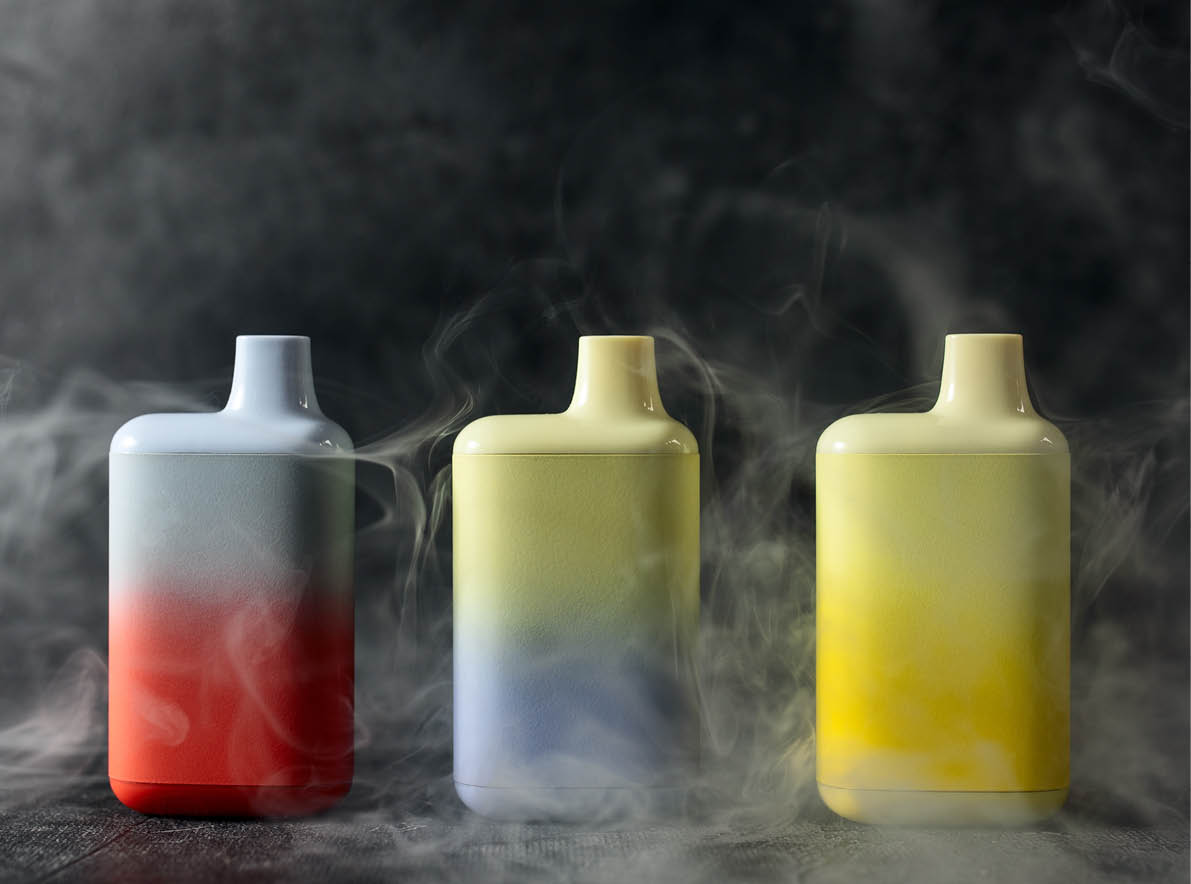 A set of multicolored disposable electronic cigarettes on a dark background stand on a table with smoke around. The concept of modern smoking, vaping and nicotine