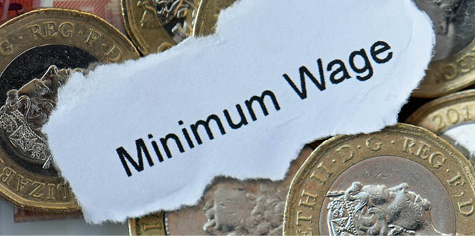 London, United Kingdom, February 1, 2024. Sterling cash bank notes and pound coins. Words Minimum Wage on piece of paper. Pay, finance, savings, money. Studio flat lay close up.