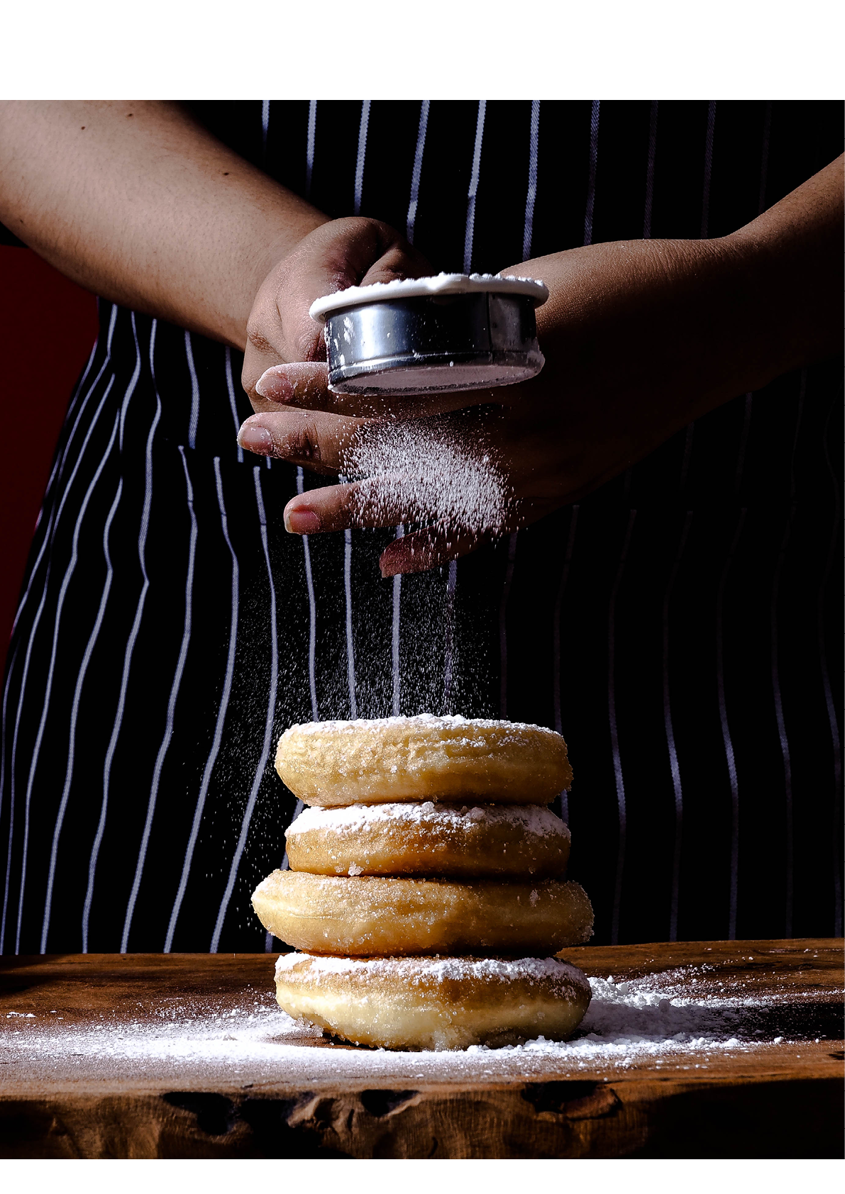 Baker decorates sweet donut with icing sugar on red background. Unhealthy food on the old wooden table with copy space. Art food. 