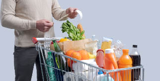 Man standing next to a full shopping cart and checking the grocery receipt