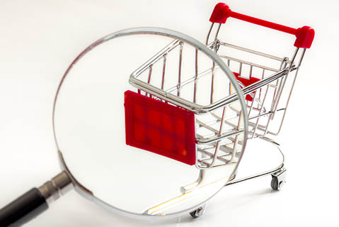 Secret shopper or mystery shopper concept with a magnifying glass and a shopping basket or trolley isolated on a white background and copy space