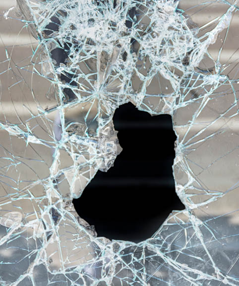 Hole in the broken glass of a shop window of a closed shop