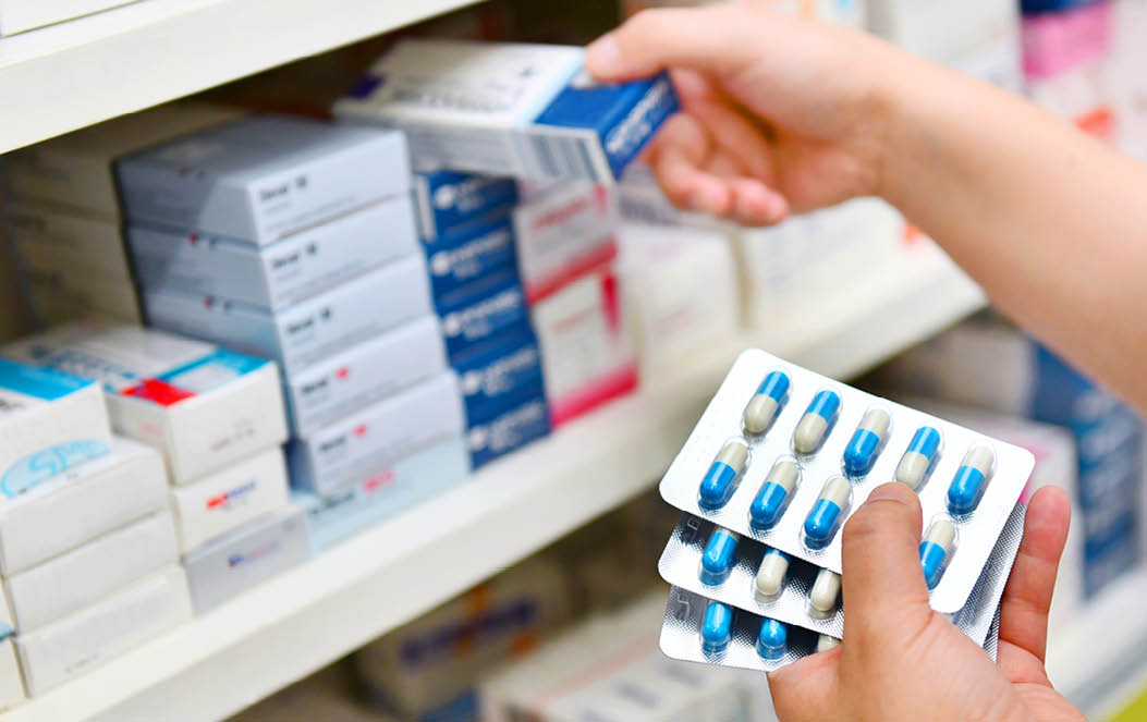 Pharmacist holding medicine box and capsule pack in pharmacy drugstore.