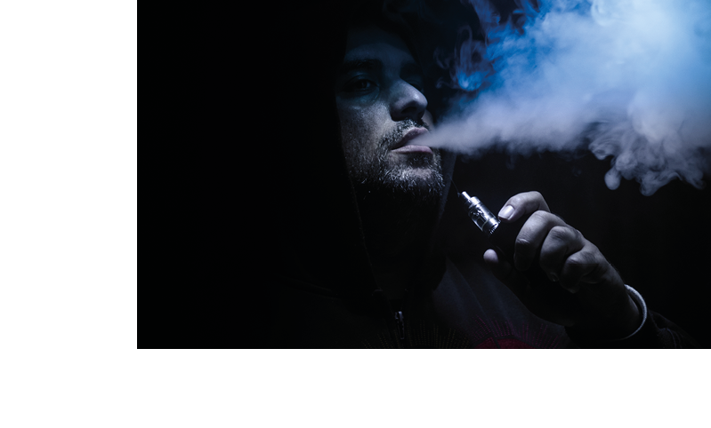 Vaping man holding a mod. A cloud of vapor. Black background. Vaping an electronic cigarette with a lot of smoke. Vape concept
