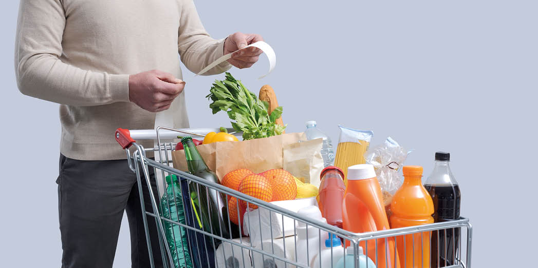 Man standing next to a full shopping cart and checking the grocery receipt