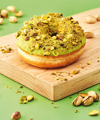 Homemade pistachio donut with nut sprinkles on a wood desk and green background