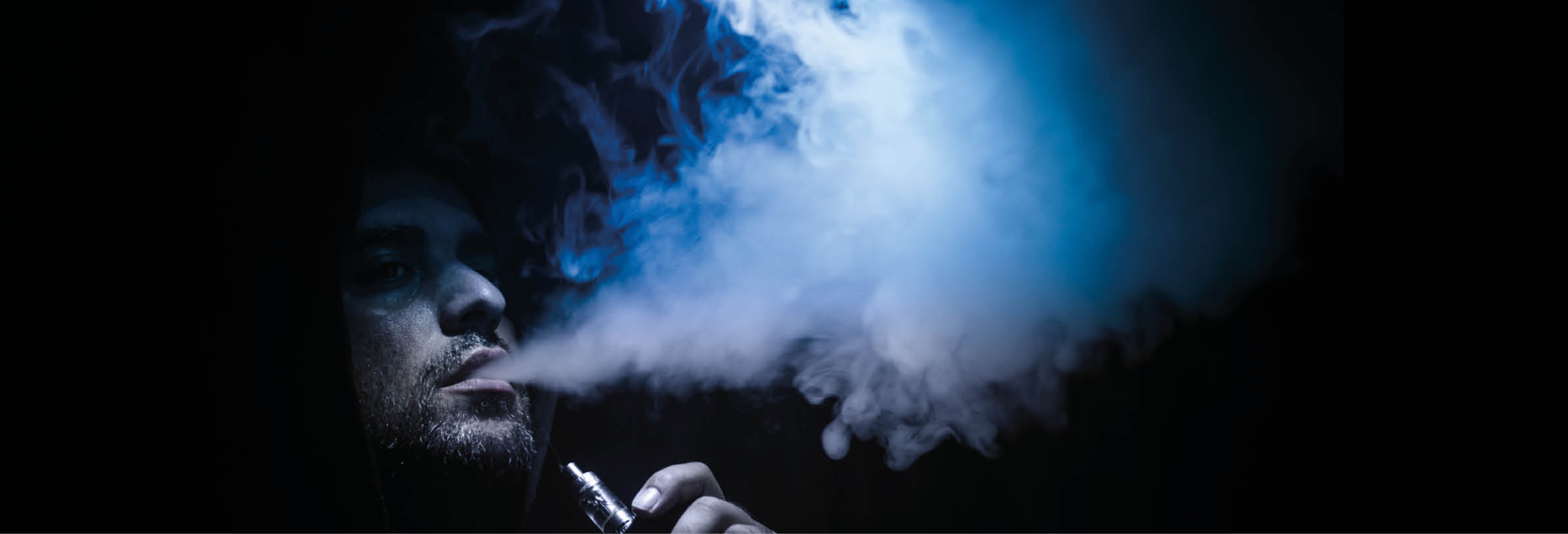 Vaping man holding a mod. A cloud of vapor. Black background. Vaping an electronic cigarette with a lot of smoke. Vape concept