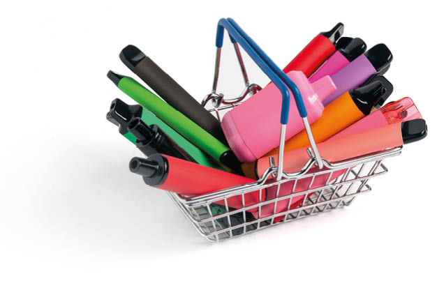 A set of colorful disposable electronic cigarettes of different shapes in a grocery basket on a white background with copy space. Concept of modern smoking.