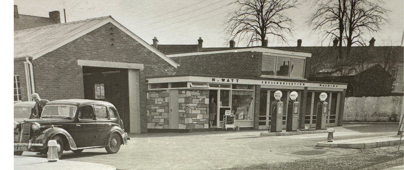 An old car is parked in front of a building, which appears to be a gas station. AI generated content