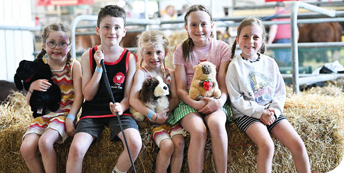 A group of children sitting on a bale of hay, holding stuffed animals. AI generated content